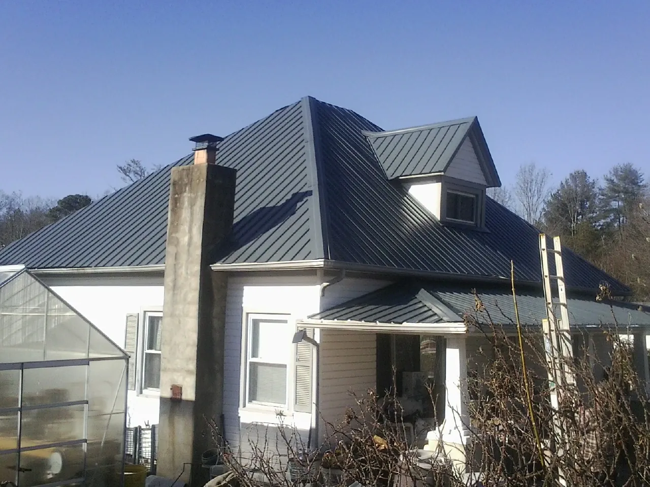 Dark blue standing seam metal roof on a white farmhouse with dormer in Amesville