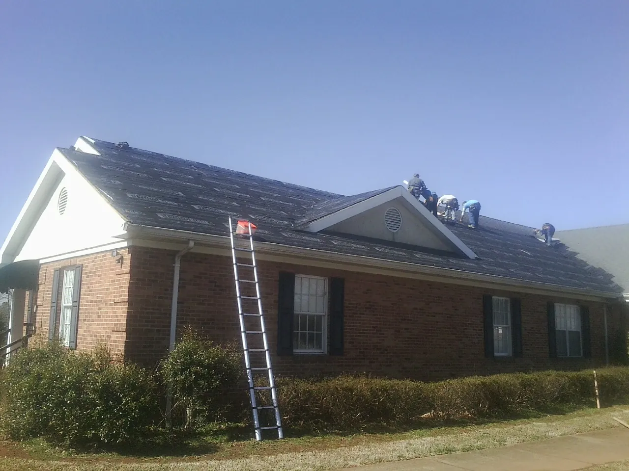 Crew tearing shingles off a brick ranch roof with a ladder set — Emergency Roof Repair work by our crew in Amesville