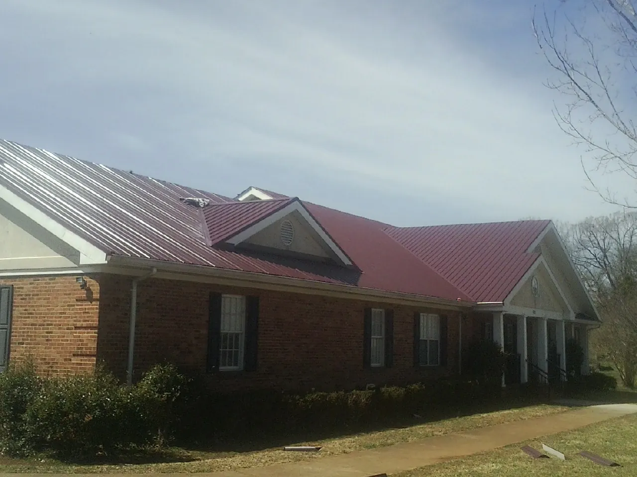 Red metal roof with gabled entries on a long brick building, from a Hail Damage Roof Repair job in Amesville