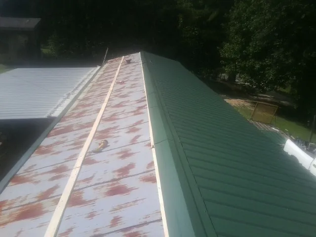 Old rusted panels beside newly installed green metal roofing — Wind Damage Roof Repair by Roofing Brothers in Amesville