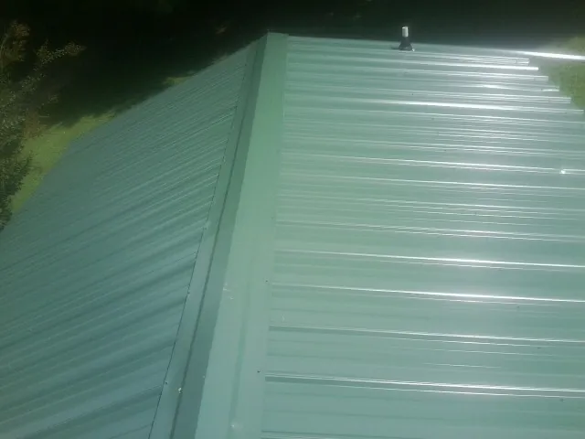 New green metal panels meeting at the ridge of a roof — Flat Roof Repair work by our crew in Amesville