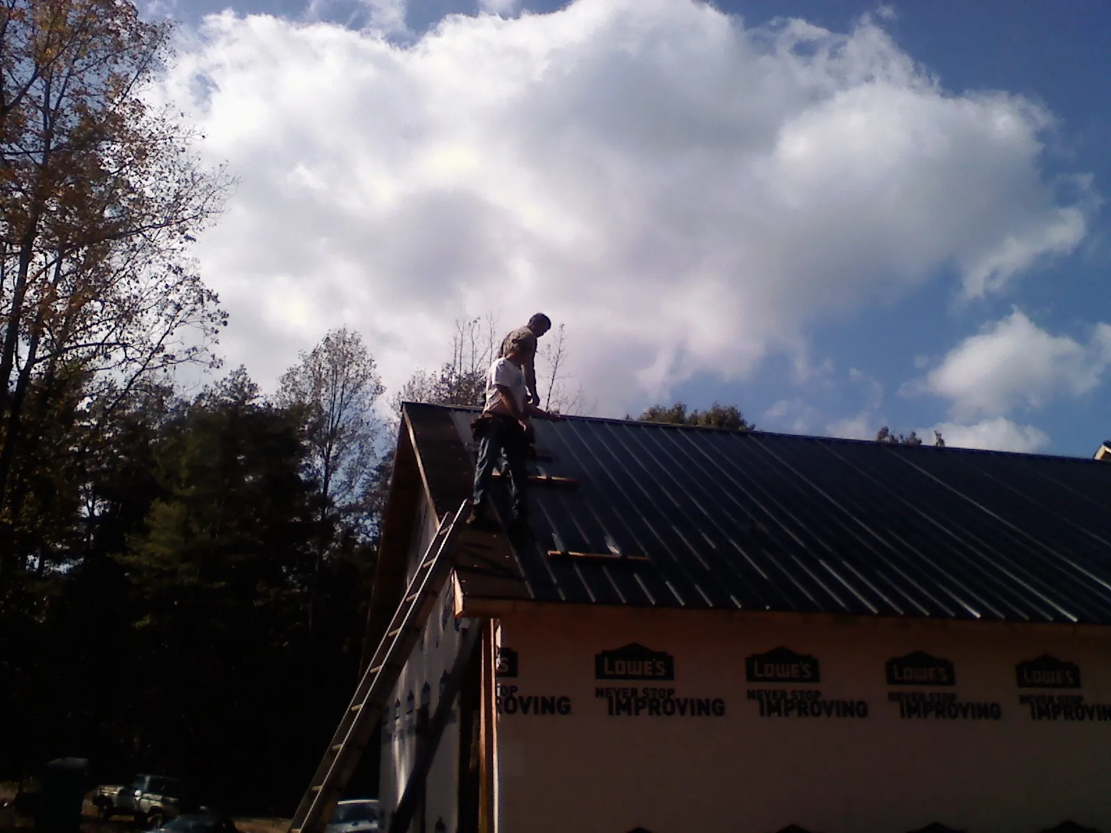 Roofer fastening dark metal panels high against a cloudy sky, from a Roof Inspection job in Amesville