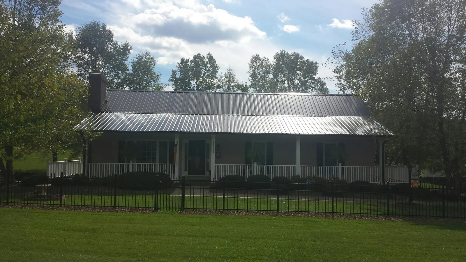 Gray metal roof on a brick ranch with a full width front porch — Gutter Guard Installation work by our crew in Amesville