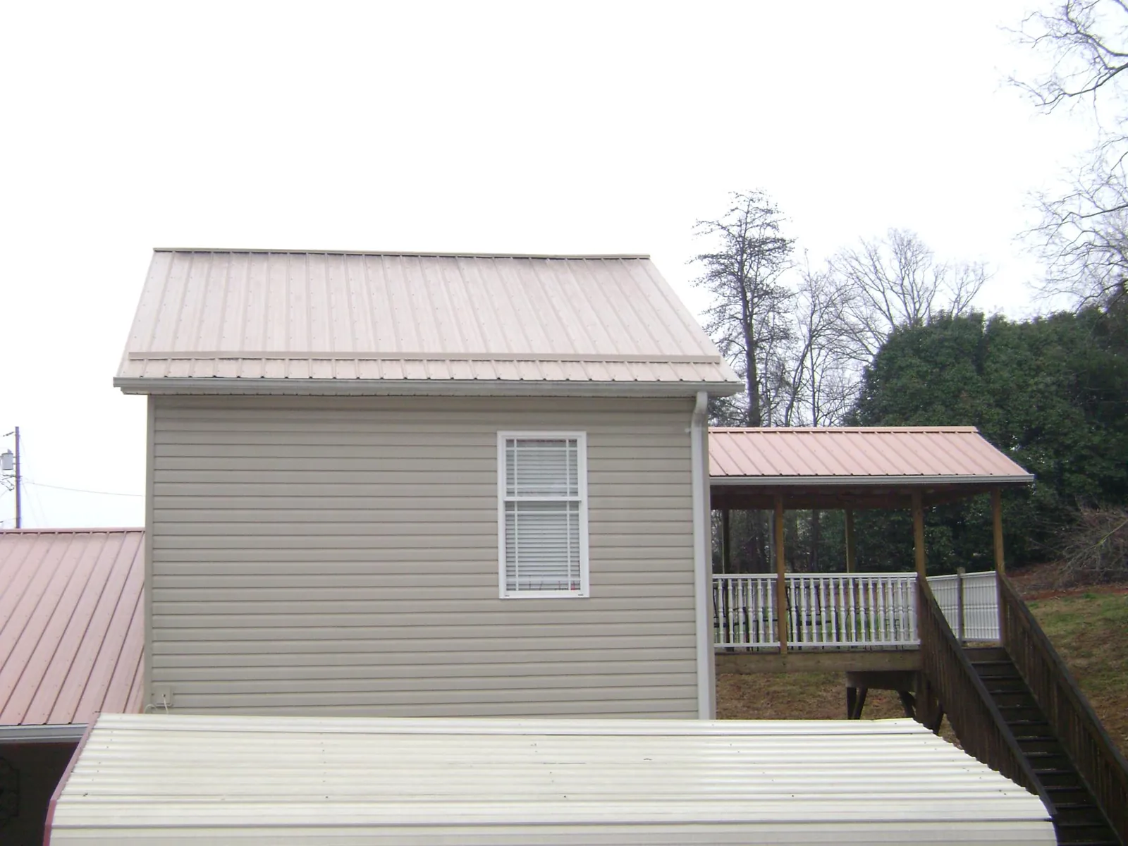 Tan metal roofs on a two story addition and attached porch, from a Roof Replacement job in Amesville